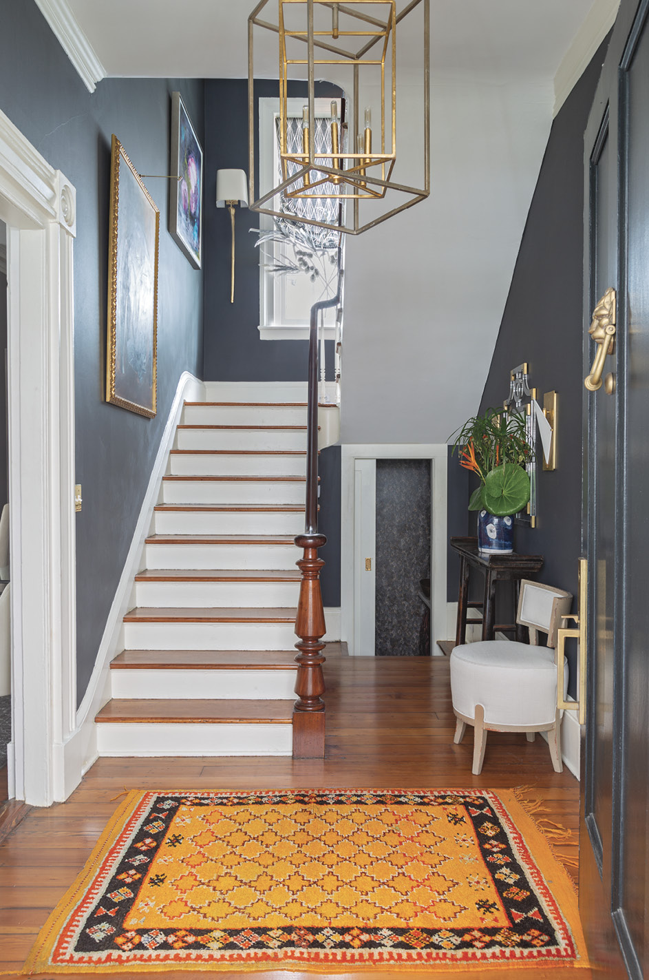 High Contrast: The entry and stairwell are painted in Benjamin Moore’s striking “Wrought Iron.” Offset by white trim and the wooden treads and handrail, the color adds personality to a utilitarian space and helps the gold accents (wall sconces and chandeliers from Circa Lighting) pop.