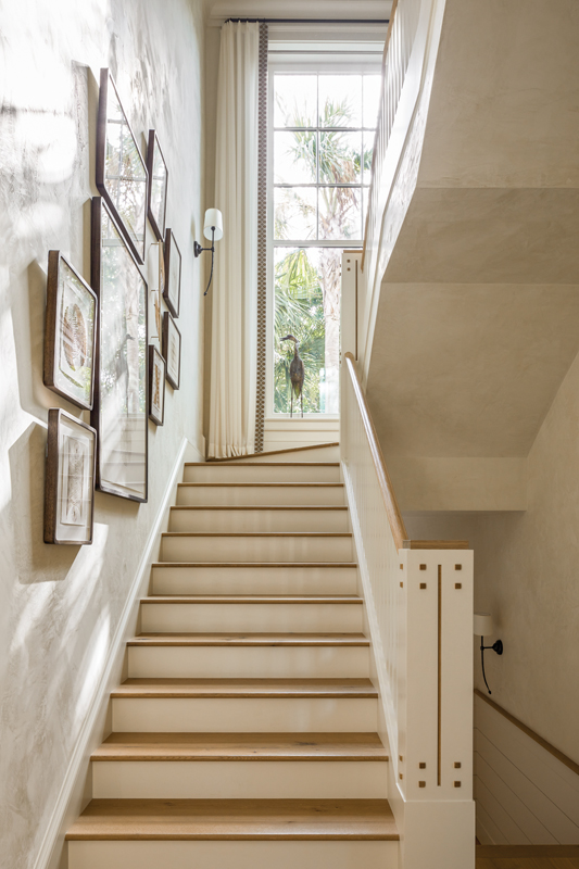 A bright stairwell adorned by a gallery wall leads to the second floor, where a hallway and sitting room connect the two bedrooms.