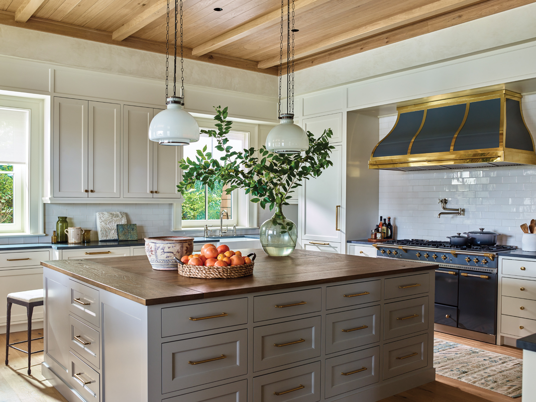 Custom plaster walls surround the space and continue into the kitchen, where cabinets painted in Benjamin Moore “Gray Mist” showcase a Lacanche range and a large, wood-topped island.