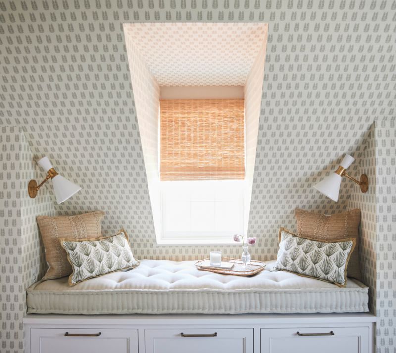 Two articulating “Liam” wall sconces from Visual Comfort, in brass with matte white shades, illuminate a cozy daybed, creating a perfect reading nook.