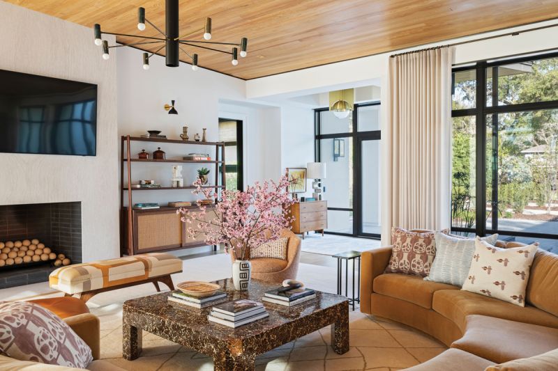 Warming Trend: The open plan living room/dining room/kitchen is dominated by a shapely Thayer Coggin sectional, selected by designer Allison Elebash to break up the space and create a more intimate seating area. The camel-colored mohair sofa is complemented by a circa-1970 Enrique Garcel coconut shell coffee table. The warm, natural colors align with the cypress ceiling and views of the oak trees beyond.