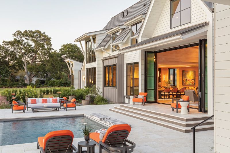 Floor-to-ceiling, folding glass doors bring the living room of this modern farmhouse right to the edge of the pool deck.