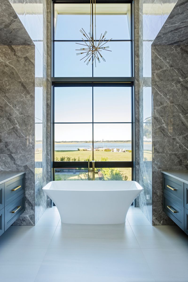 The primary bedroom suite boasts stunning vistas, including from this luxurious freestanding tub surrounded by porcelain walls and floor tile that add drama to the space.