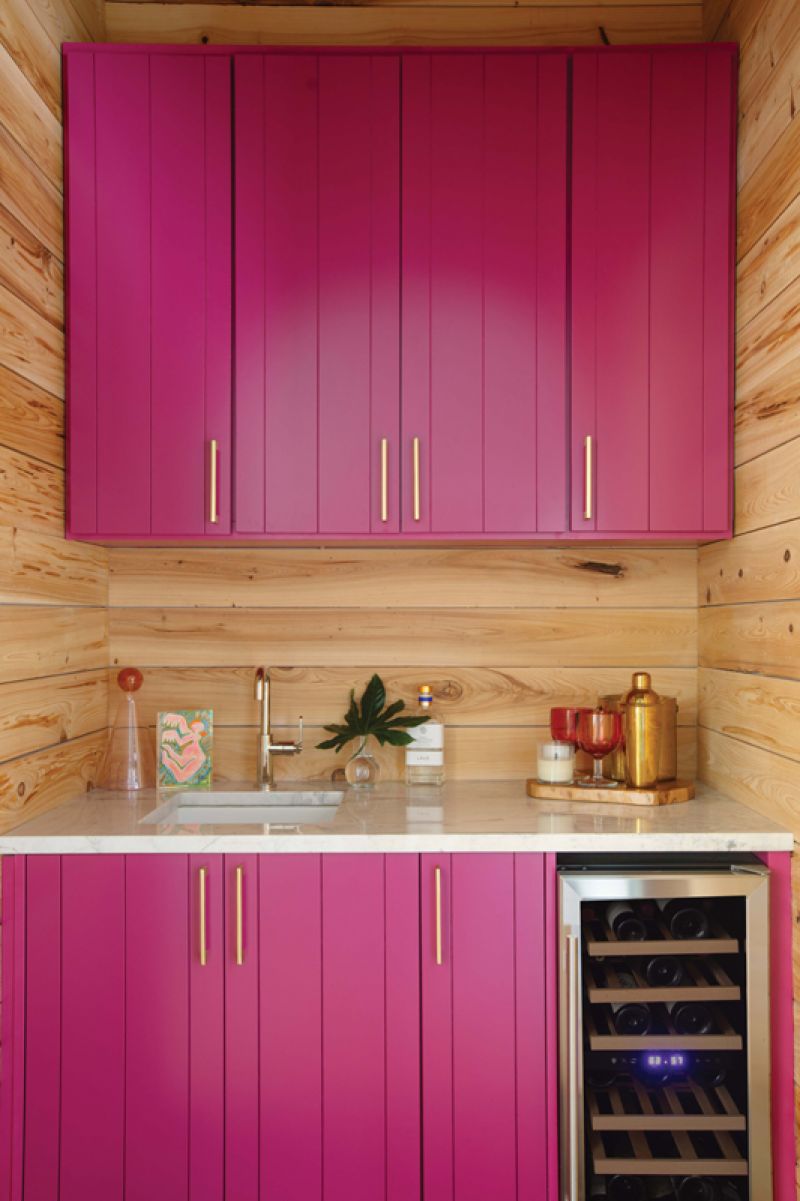 Between the rooms, a small bar area is accessed through an arched entry. Here, interior designer Becca Jones added a fun pop of color to the cabinets with Sherwin Williams “Forward Fuchsia.”