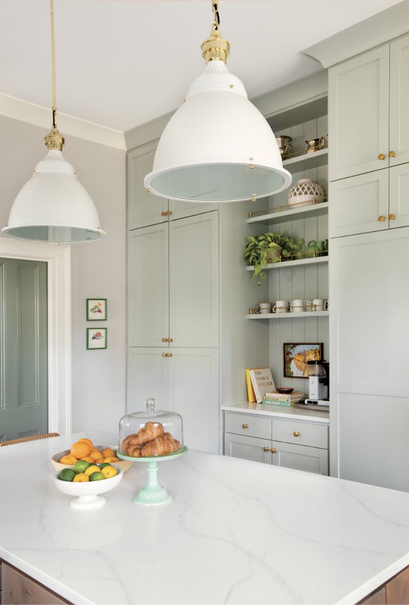 The space between: A coffee nook with slim, brass-accented shelves hung on a shiplap-covered wall breaks up the expansive floor-to-ceiling pantry that also houses a full fridge and freezer behind its Benjamin Moore “Gray Wisp”-painted cabinets. Pulls from Water Street Brass complement the shelves and the oversized Restoration Hardware pendants hanging over the quartzite-topped island.