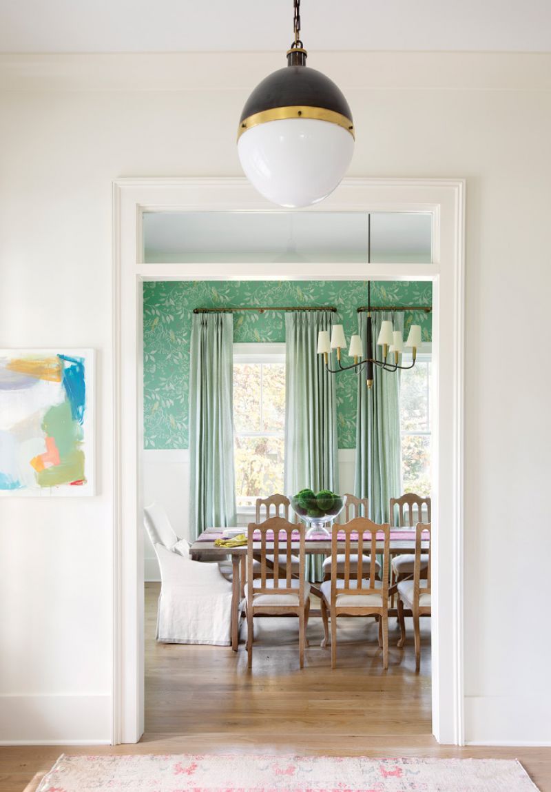 Color Play: An Emily Brown abstract painting from Charleston Artist Collective and a pink rug from Zuma Imports add pops of color in the main entry hall, which is painted a calming “White Dove” from Benjamin Moore. A bold light fixture from Circa Lighting, framed between the extra wide cased opening with transom window, adds a touch of drama to the dining room.