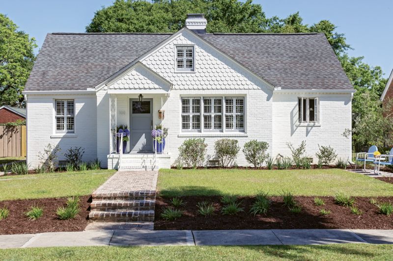 FRESH FACED: To camouflage brick patchwork and better blend the scallop detailing with the rest of the façade, homeowner Rachel Levkowicz had the exterior coated in Benjamin Moore’s “White Dove,” using Sherwin Williams’ “African Gray” as an accent hue. Other Side of the River constructed the property’s new walkway. “It’s one of my favorite things I added to the house,” says Rachel.