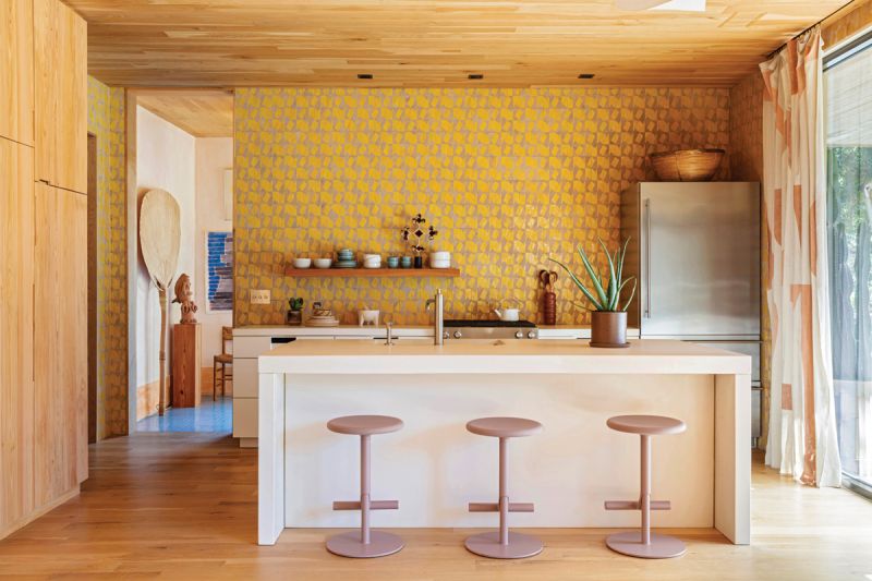 Geometric zellige tiles in a creamy yellow create a statement wall where a lack of upper cabinets and range hood allows the tile to shine. A single cypress shelf showcases Mexican pottery from Taller Experimental de Cerámica in Coyoacán. The concrete island and countertops add to the casual vibe, while a Waterworks faucet creates a sculptural moment. The cypress pantry, designed by Hranowsky and built by Scott Meara, includes customized drawers and an appliance garage.