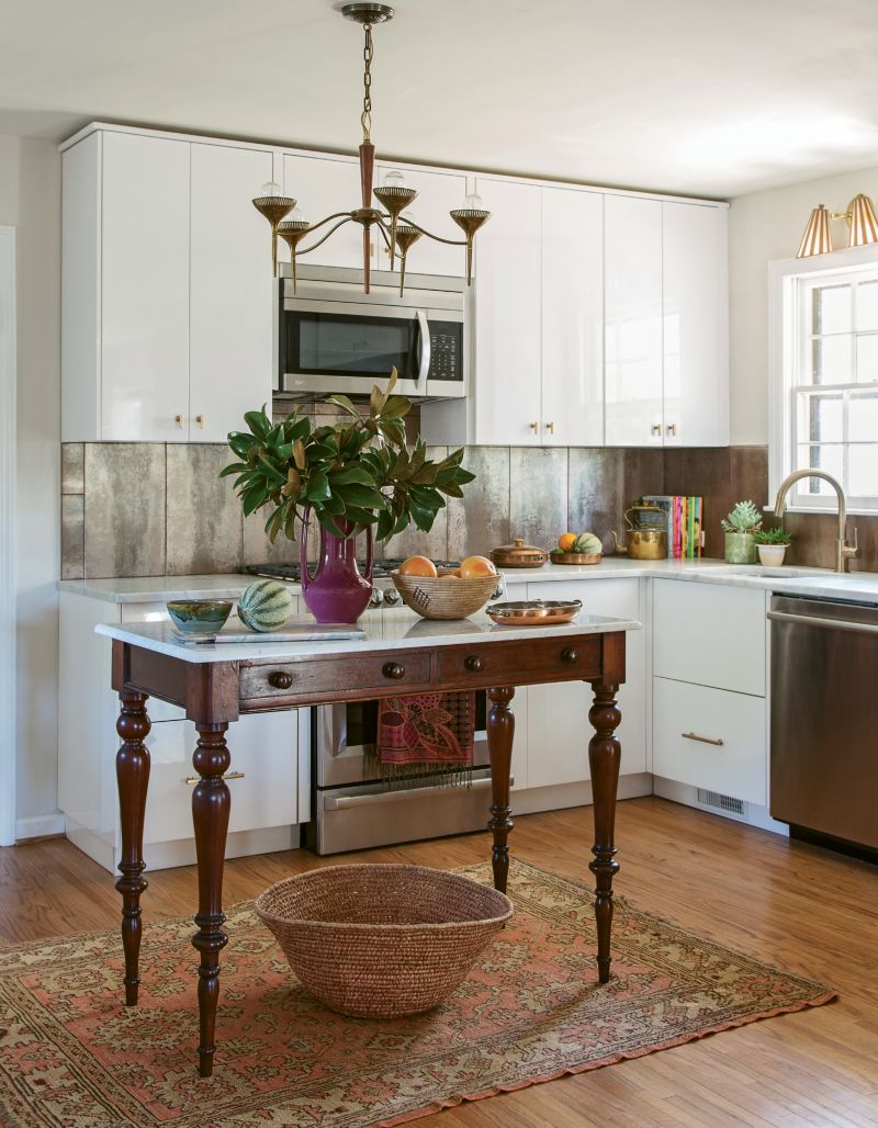 FRESH TAKE: High-gloss cabinets and a cool coppery backsplash help modernize the retro kitchen. But antique pieces—such as a brass-and-wood mid-century light fixture and a marble-top table reimagined as an island—lend vintage charm that’s cohesive with the rest of the abode.