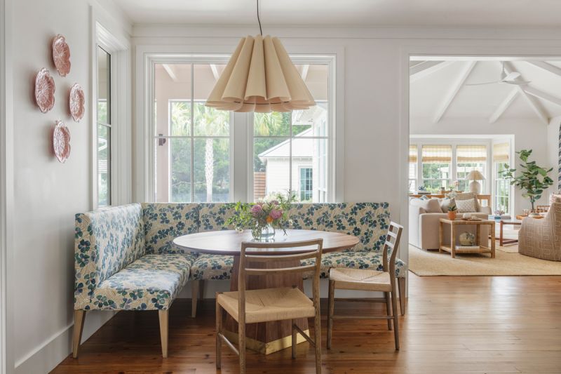 The adjoining breakfast room features a custom banquette covered in fabric from Brook Perdigon Textiles and a Benjamin Paul Studio walnut table, topped by a “Lora” pendant from Lumens.
