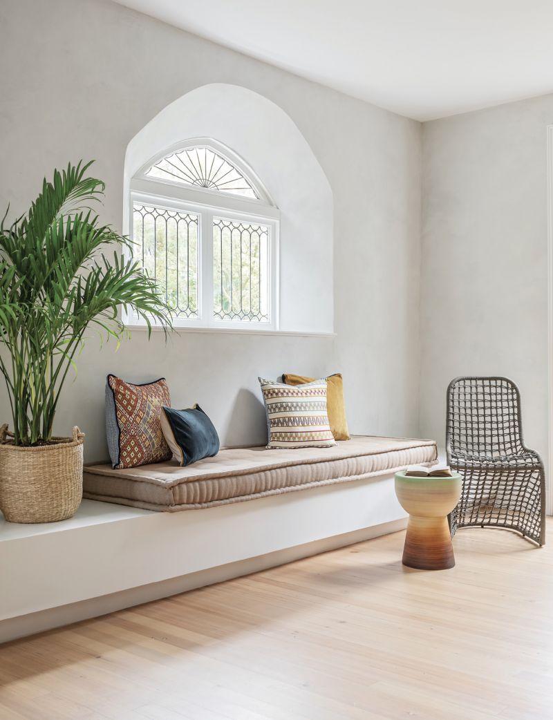 Modern Mood:  A renovation merged the kitchen and porch to create a larger, more modern space. This wall, with its original Gothic-style window, was once crammed with upper and lower cabinets and a long counter. Now it emanates calm minimalism while retaining its historical feel and adding seating, thanks to a built-in banquette.