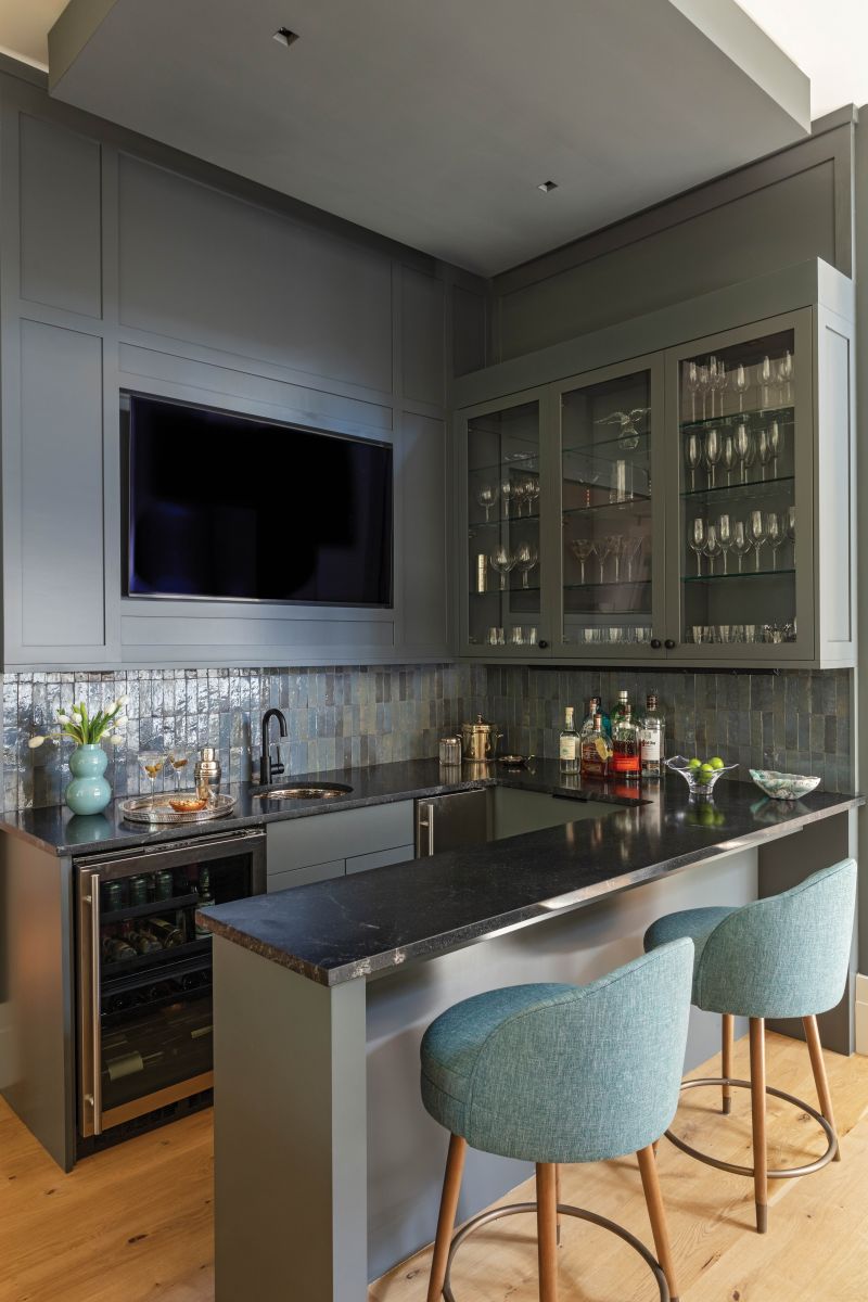 Moody Hues: Painted in Farrow &amp; Ball “Down Pipe,” a deep charcoal with hints of blue, the bar adds an eye-catching element in the bright open living area. A tray ceiling and handmade Moroccan Zellige tile complete the dramatic look.