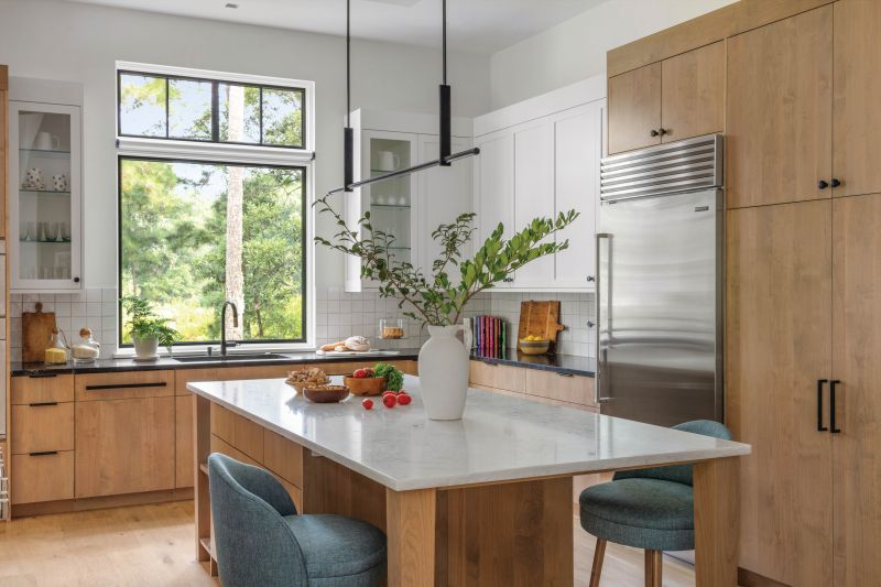 Taking advantage of the ample natural light, the kitchen combines alder wood cabinets with Benjamin Moore “Cloud White” painted walls and upper cabinets, as well as a dramatic black Kelly Wearstler “Axis Large Linear” pendant.
