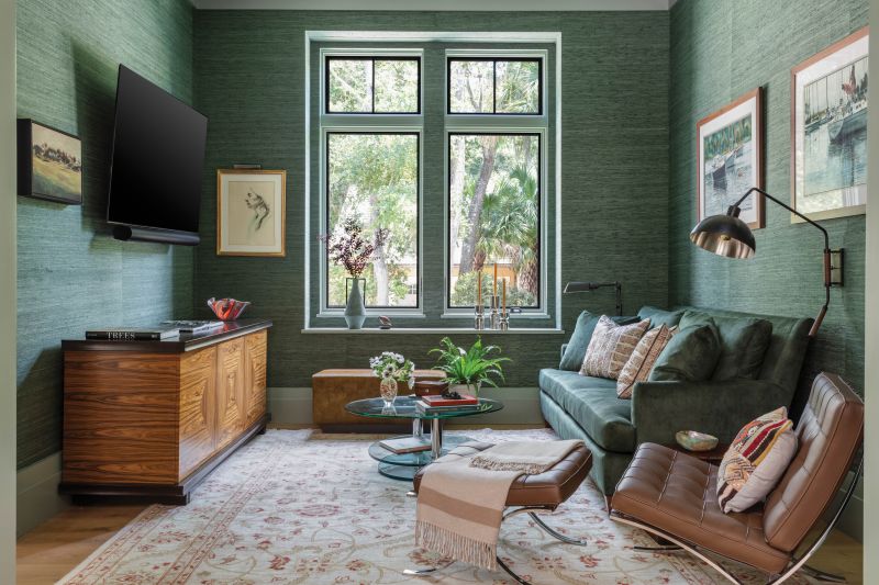 A color-drenched den sits off the primary bedroom. The cocoon-like space is enveloped in a sage green, raw silk wall covering from Phillip Jeffries with the trim, builts-ins, and ceiling all painted in a coordinating Benjamin Moore “Secret Path.” The Hickory Chair sofa is wrapped in a velvet performance fabric, and the homeowners’ Mies van der Rohe “Barcelona” chair complements the sculptural coffee table for a touch of sophistication.