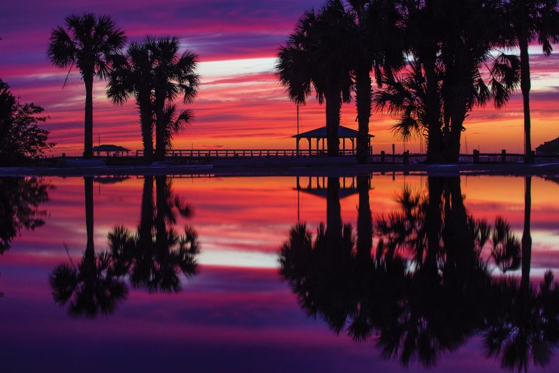 An epic April sunset over Folly River Boat Ramp reflects in the empty parking lot puddled with rainwater.