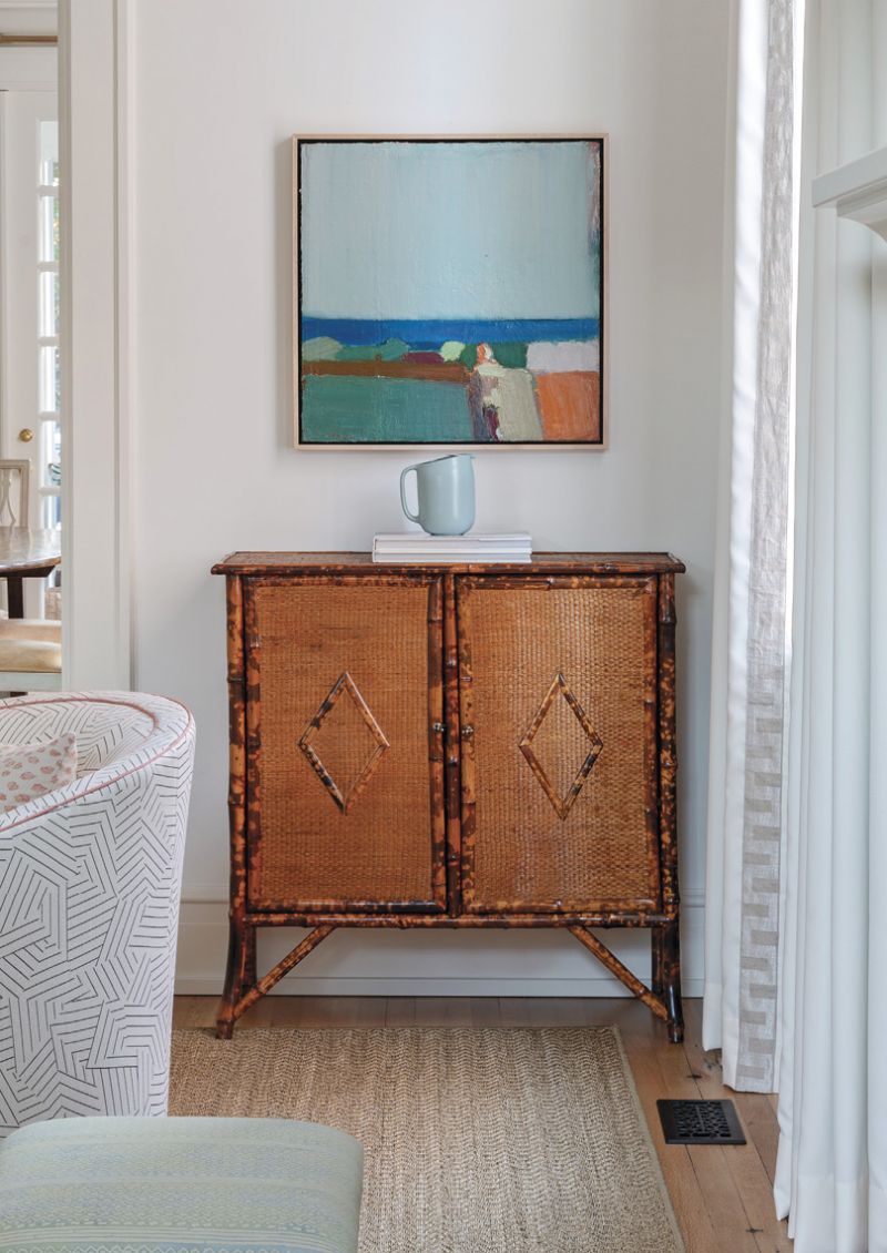 NEUTRAL TERRITORY: Benjamin Moore’s ‘Simply White’ is the backdrop for a mix of natural hues throughout the home, from white oak flooring to a Fibreworks rug, allowing certain pieces to pop, such as this bamboo cabinet from Acquisitions and Sandy Ostrau abstract oil painting from Meyer Vogl Gallery.