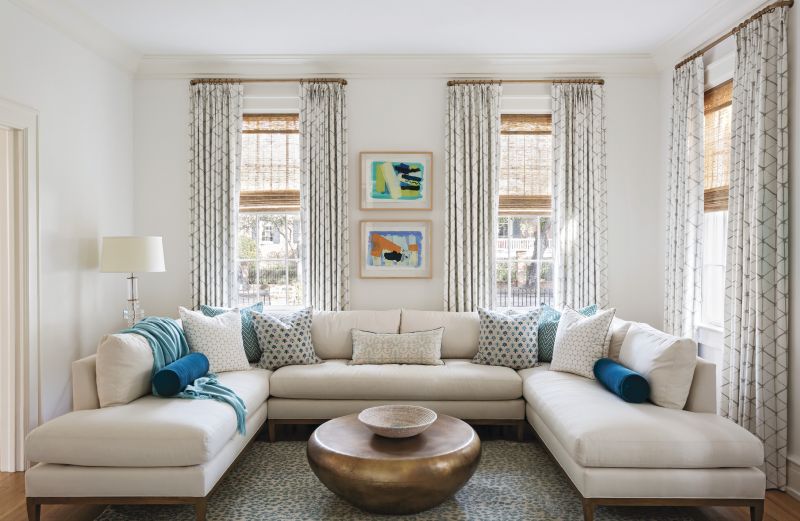 COORDINATED COMFORT: In the laid-back but still stylish family room, a burnt brass-finished cocktail table from Arteriors fills the space in front of the U-shape sectional sofa from Lee Industries. Sally King Benedict paintings, along with scattered throw pillows encased in fabrics from Pierre Frey, Mally Skok Design, and Villa Nova, add color.