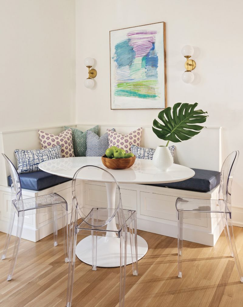 Pops of pastel color are introduced in the aqua-colored pendant lights from Urban Electric, a vintage rug, and a Sally King Benedict painting above the deep blue banquette.