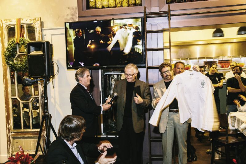 Maverick Southern Kitchens partners David Marconi and Dick Elliott present Lee with a chef’s coat “signed by so many wonderful people and I can’t ever wear it or wash it,” he says.